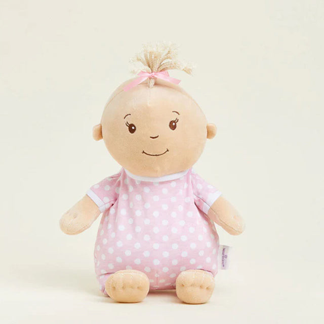 Stuffed toy baby doll with pink polka dot outfit on a light beige background