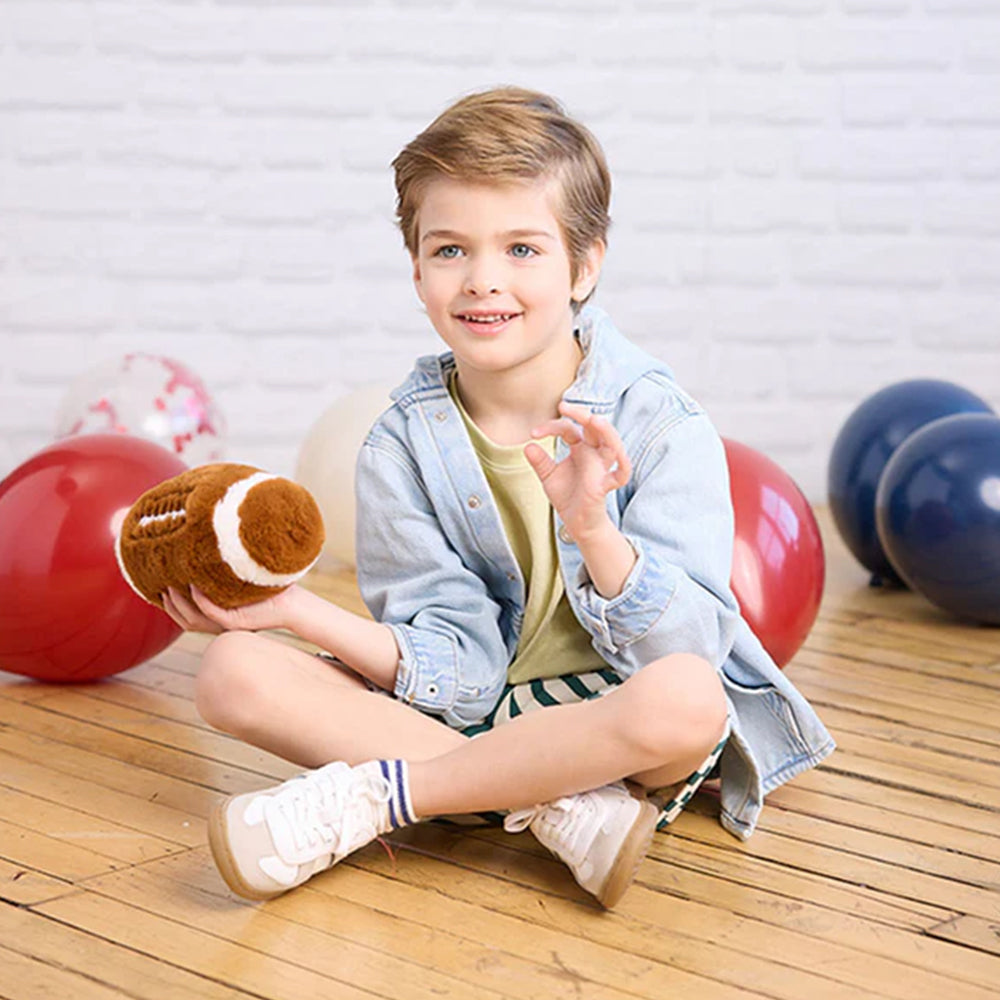 Child sitting on a wooden floor holding a football with colorful balls in the background