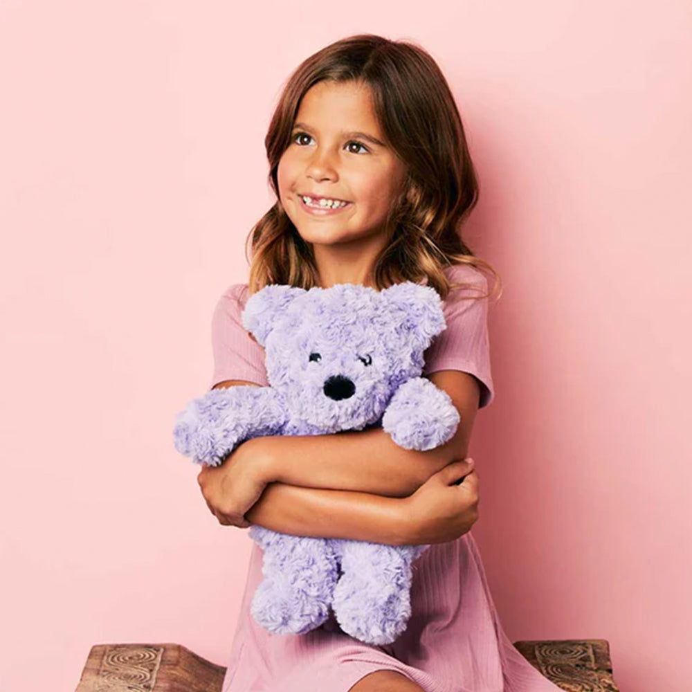 Young girl holding a purple teddy bear against a pink background